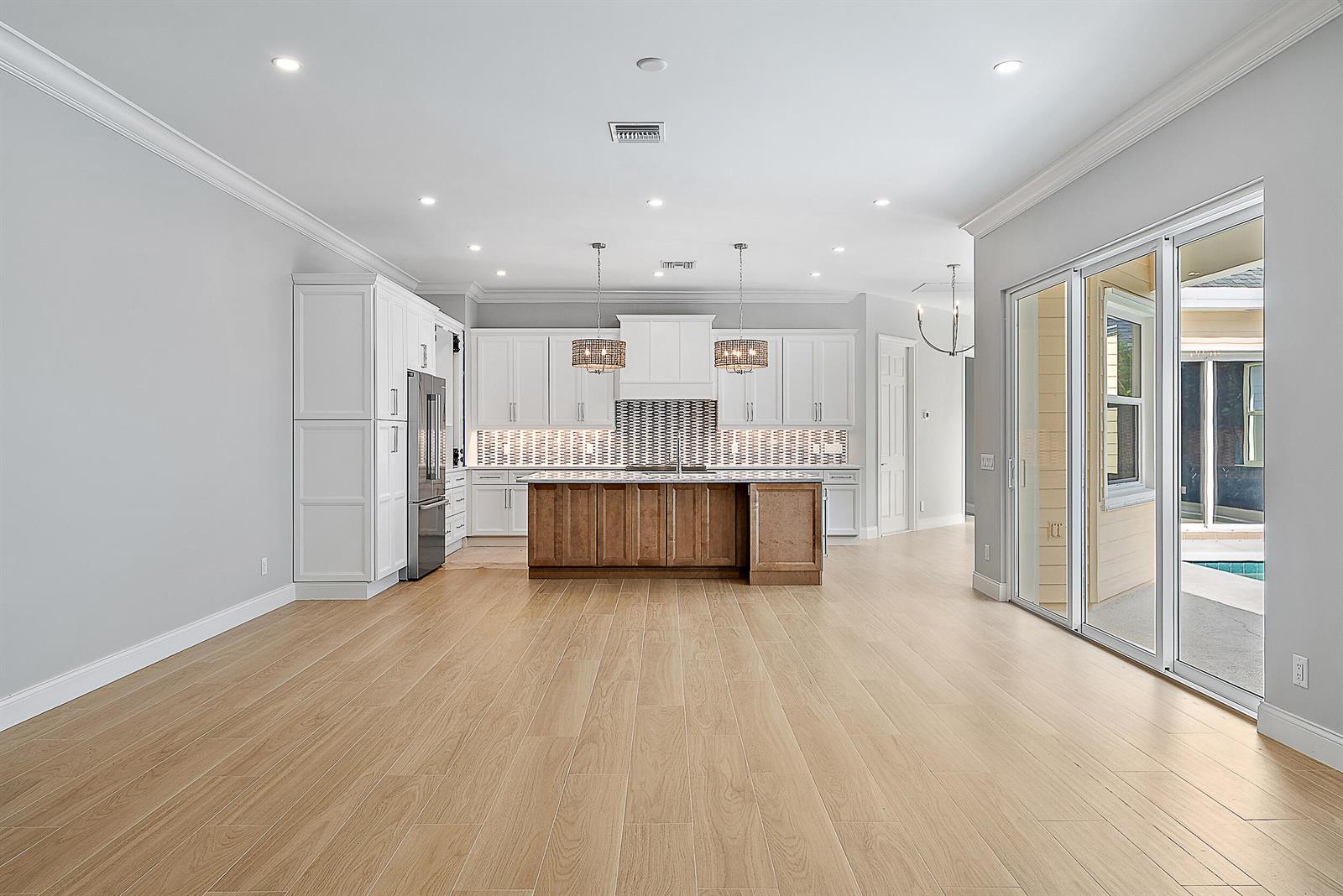 A kitchen features white cabinetry, a wood-toned island, and sliding glass doors leading outside — 248 Honeysuckle Drive, Jupiter FL 33458, JUPITER, FL