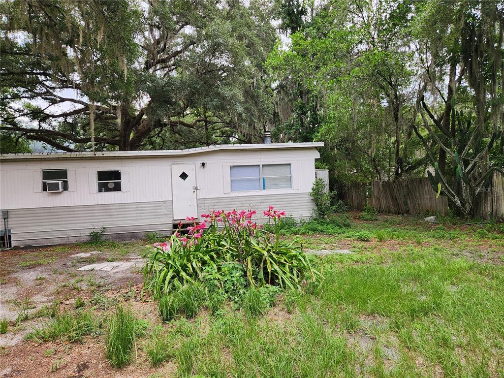A single-story mobile home sits on a grassy lot surrounded by large, moss-draped trees — 24815 AUDREY ROAD, LAND O LAKES, FL
