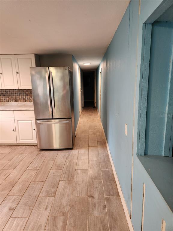 A kitchen with white cabinets and a stainless refrigerator leads into a narrow hallway — 24815 AUDREY ROAD, LAND O LAKES, FL