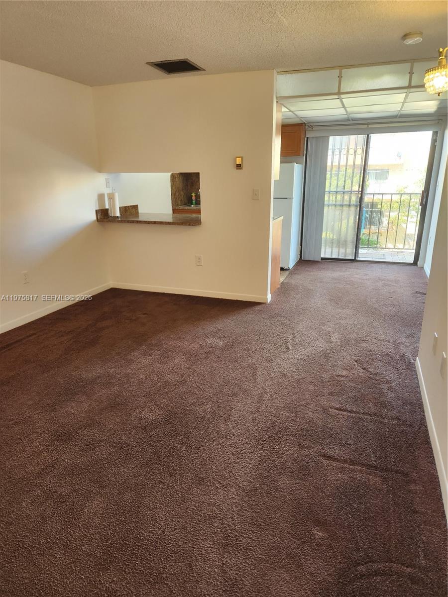 This living room features brown carpeting, a kitchen pass-through window, and a sliding glass door — 777 SW 9th Ave # 301, Miami FL 33130, MIAMI, FL