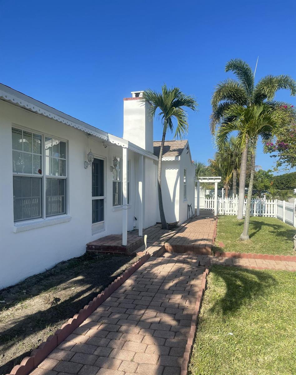A white house with a brick walkway, a chimney, and palm trees under a blue sky — 255 Foresteria Drive, Lake Park FL 33403, LAKE PARK, FL