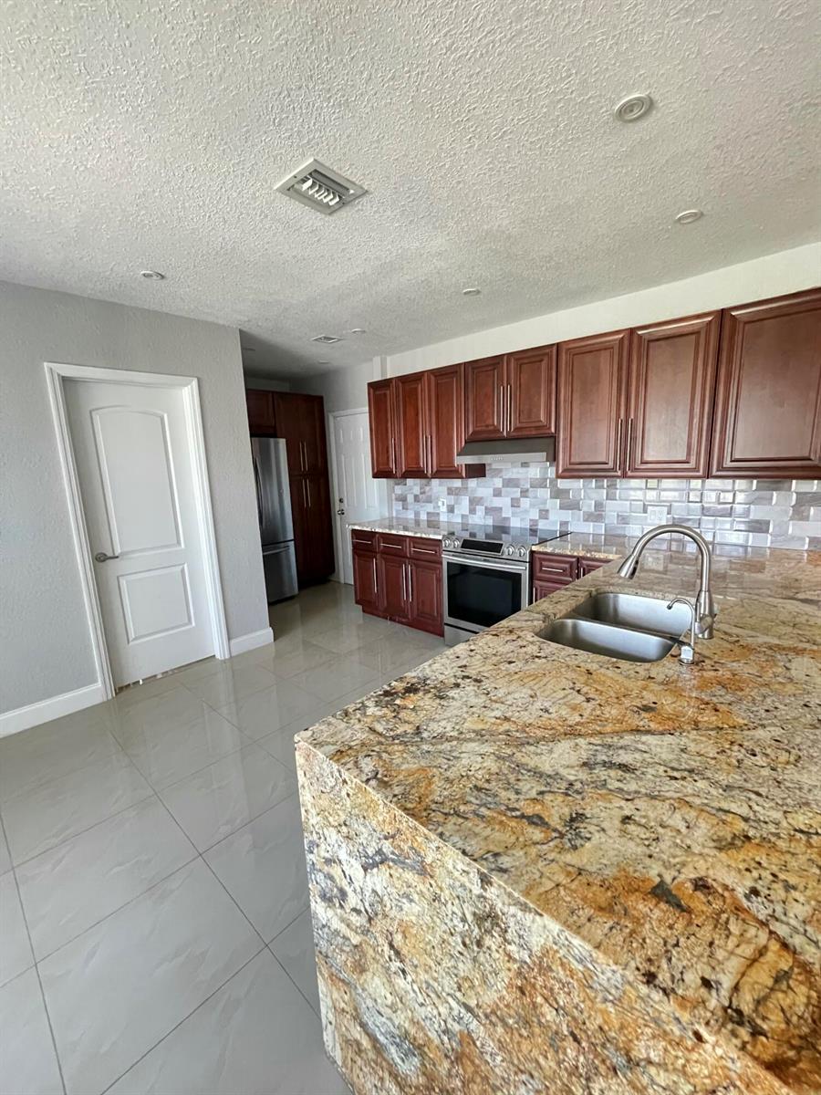A kitchen features dark wood cabinets, granite countertops, a stainless steel stove, and tile flooring — 255 Foresteria Drive, Lake Park FL 33403, LAKE PARK, FL