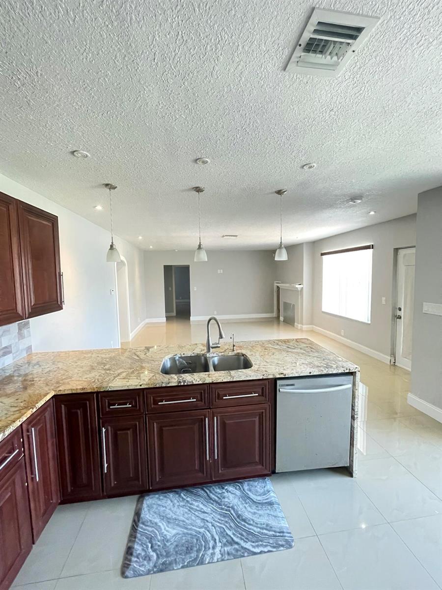 A kitchen with dark wood cabinets, granite countertops, and a stainless steel dishwasher — 255 Foresteria Drive, Lake Park FL 33403, LAKE PARK, FL