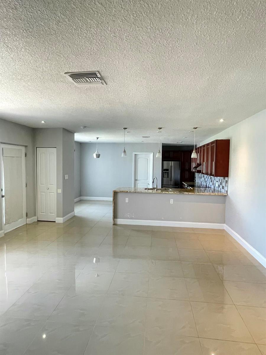 An open-concept kitchen with dark wood cabinets and a granite breakfast bar overlooks a room — 255 Foresteria Drive, Lake Park FL 33403, LAKE PARK, FL