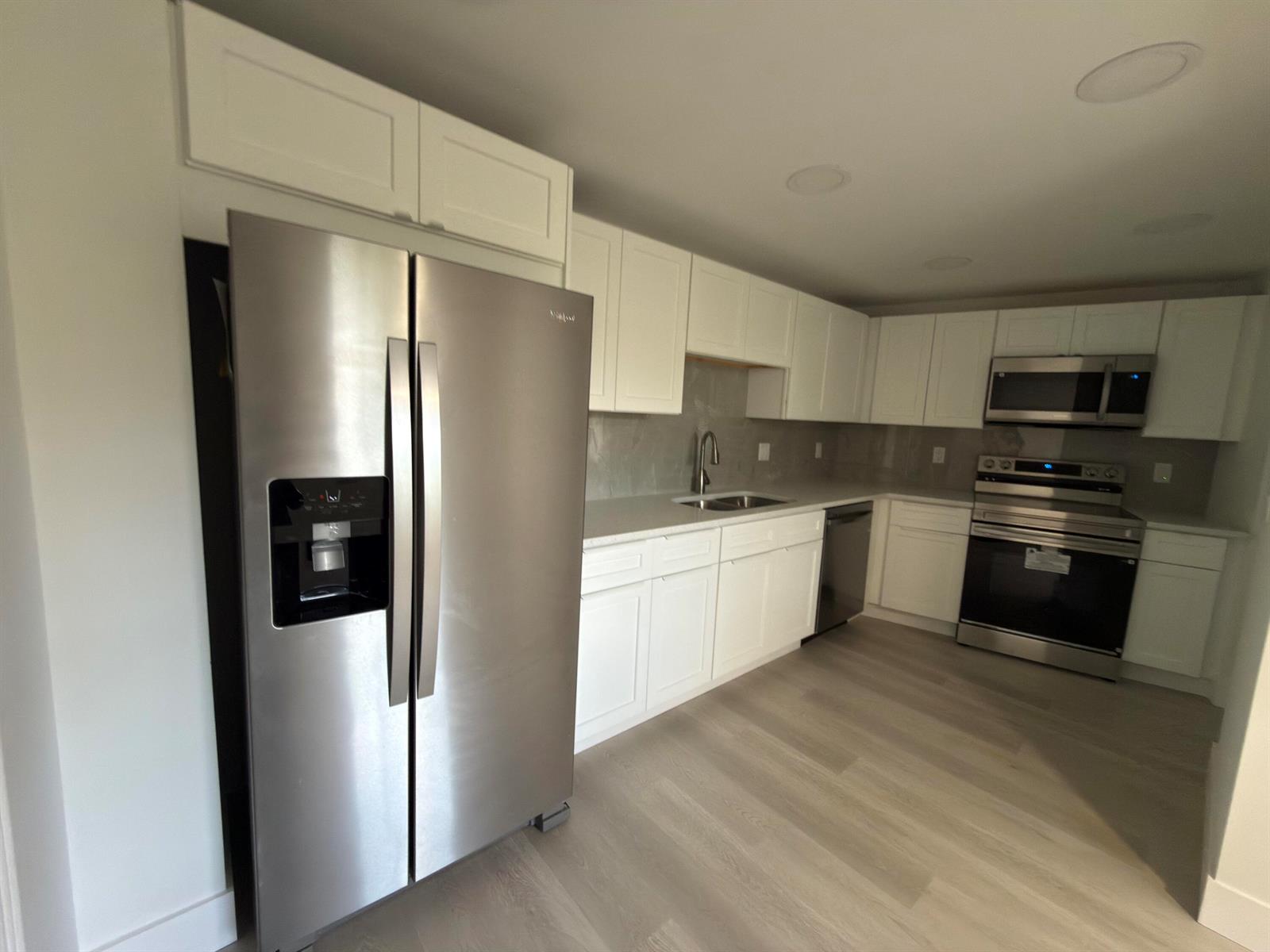 A modern kitchen features white cabinetry, stainless steel appliances, and light-colored wood-look flooring — 625 Oaks Drive # 305, Pompano Beach FL 33069, POMPANO BEACH, FL
