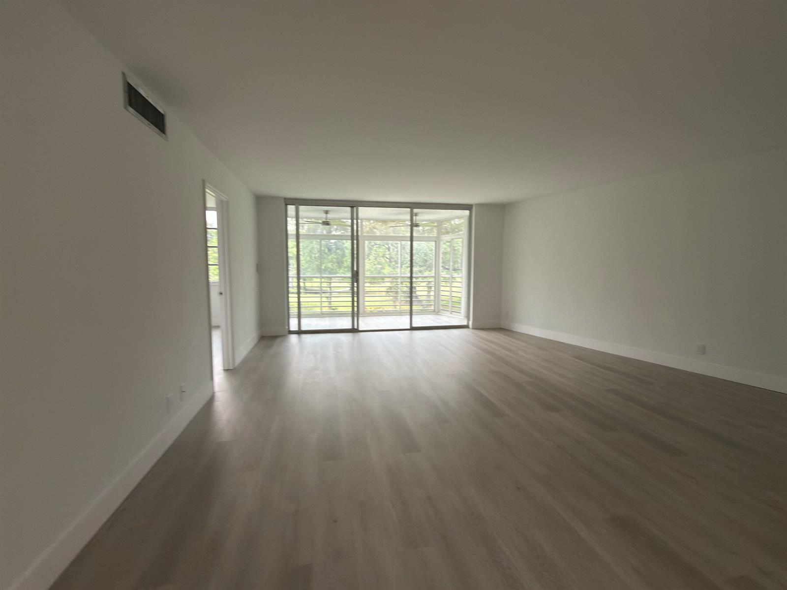An empty living room with light wood-look flooring, white walls, and a sliding glass door — 625 Oaks Drive # 305, Pompano Beach FL 33069, POMPANO BEACH, FL