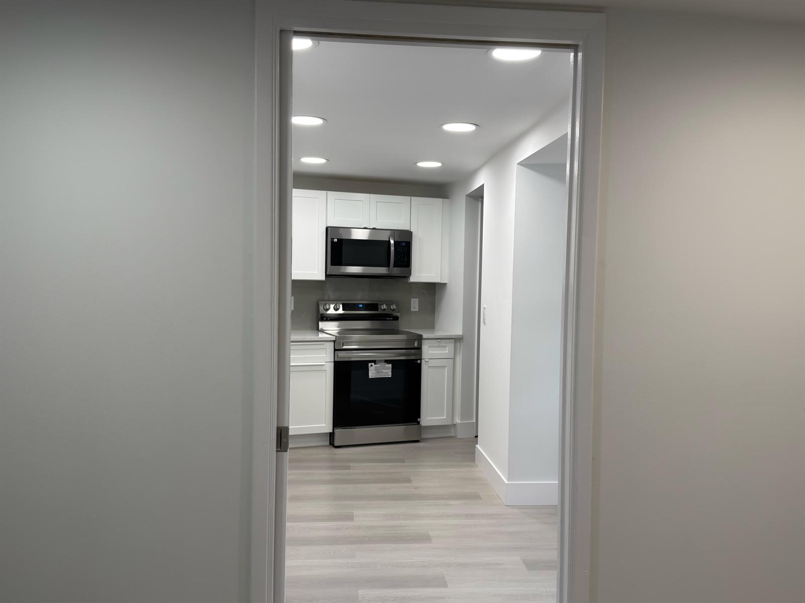 A view through a doorway into a kitchen with white cabinets and stainless steel appliances — 625 Oaks Drive # 305, Pompano Beach FL 33069, POMPANO BEACH, FL