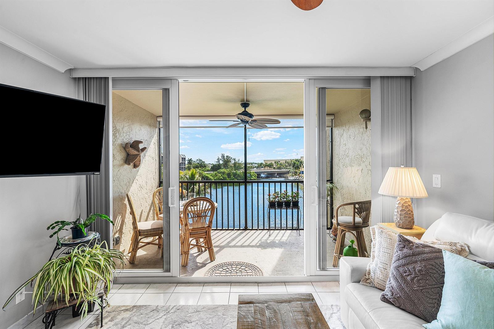 A living room with a white sofa and television opens to a balcony overlooking water — 7 Royal Palm Way # 507, Boca Raton FL 33432, BOCA RATON, FL