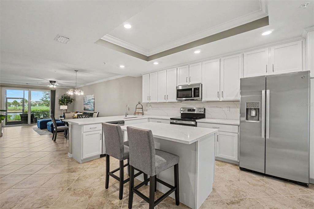 A modern kitchen with white cabinets, stainless steel appliances, and a central island with seating — 16000 GRASSLAND LANE UNIT 3112, PUNTA GORDA, FL