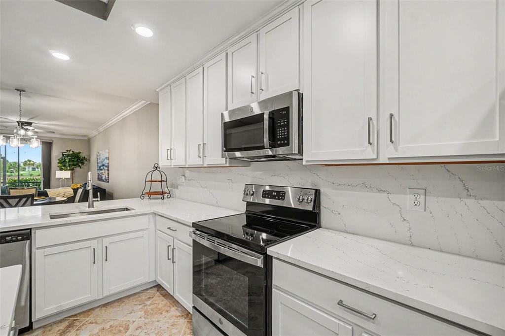 A kitchen features white cabinets, stainless steel appliances, and white quartz countertops with grey veining — 16000 GRASSLAND LANE UNIT 3112, PUNTA GORDA, FL