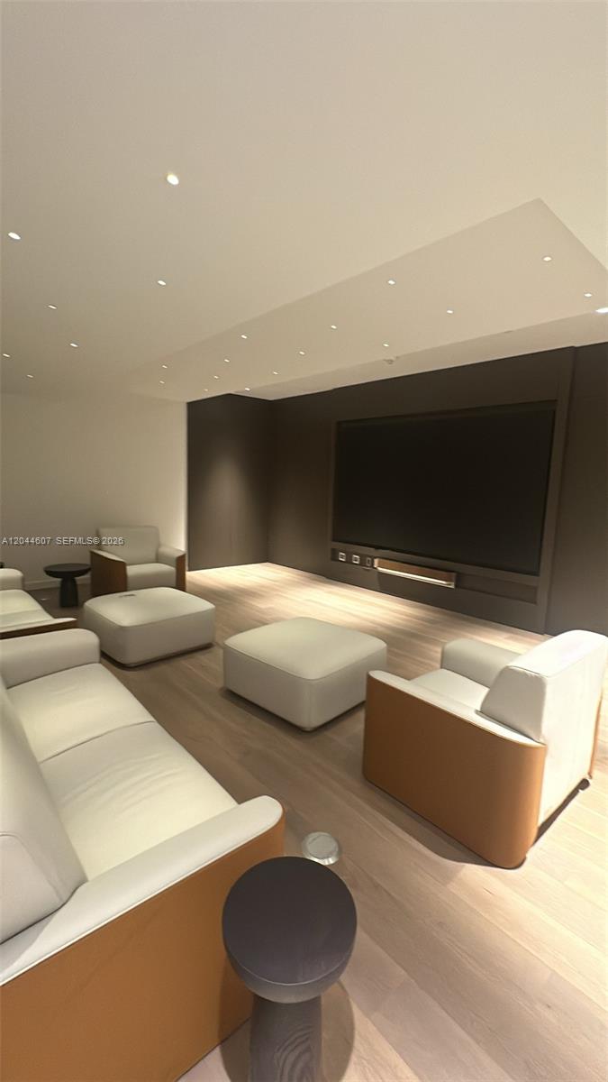 This modern media room features light wood flooring, white leather seating, and a large television — 300 Biscayne Blvd Way # 1909, Miami FL 33131, MIAMI, FL