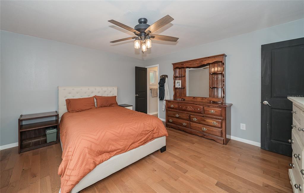 A bedroom features a bed with orange bedding, a wooden dresser with a mirror, and hardwood floors — 1404 REDBUD CIRCLE, PLANT CITY, FL