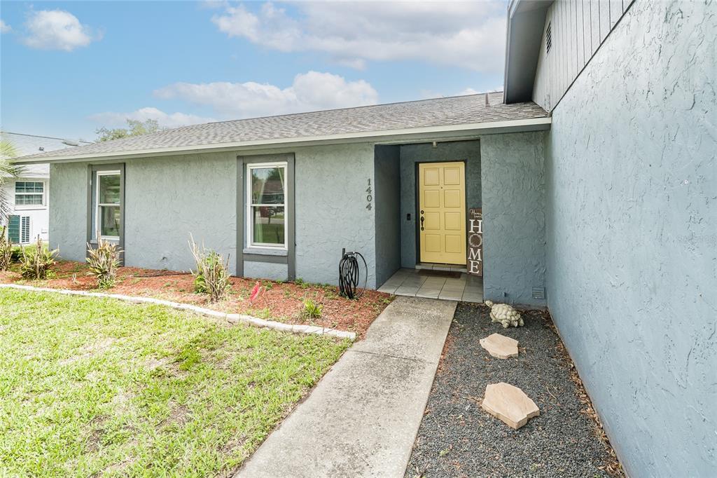 A light blue house exterior features a yellow front door and a concrete walkway — 1404 REDBUD CIRCLE, PLANT CITY, FL