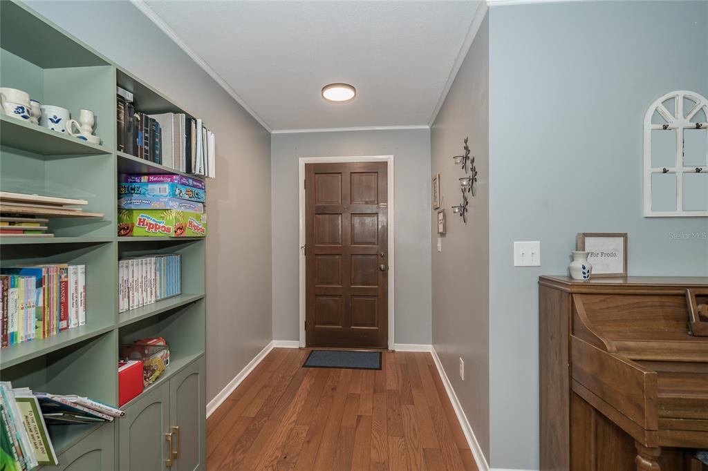 An entryway features hardwood floors, a wooden front door, a green bookshelf, and a piano — 1404 REDBUD CIRCLE, PLANT CITY, FL