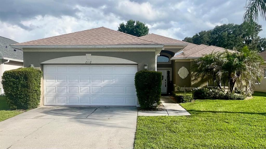 A single-story house with a two-car garage, a tan stucco exterior, and a palm tree — 2112 BUNKER VIEW COURT, KISSIMMEE, FL