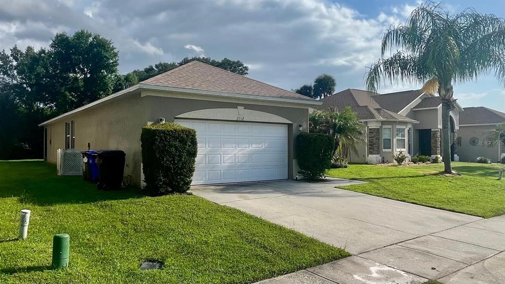 A single-story house with a white garage door, a concrete driveway, and a palm tree — 2112 BUNKER VIEW COURT, KISSIMMEE, FL