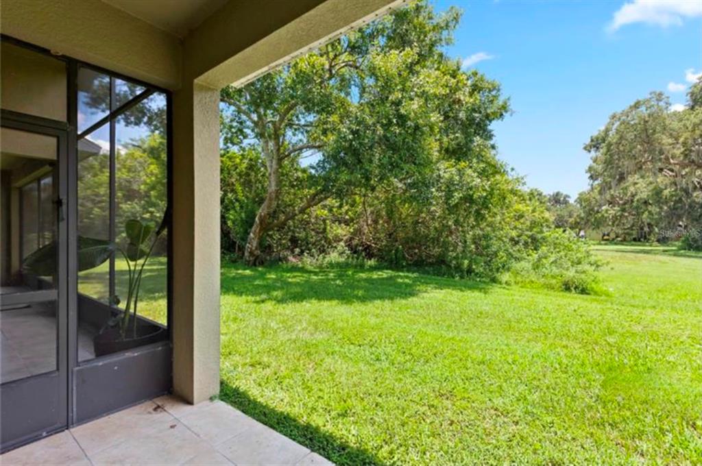 A covered patio overlooks a grassy backyard with mature trees under a blue sky — 2112 BUNKER VIEW COURT, KISSIMMEE, FL