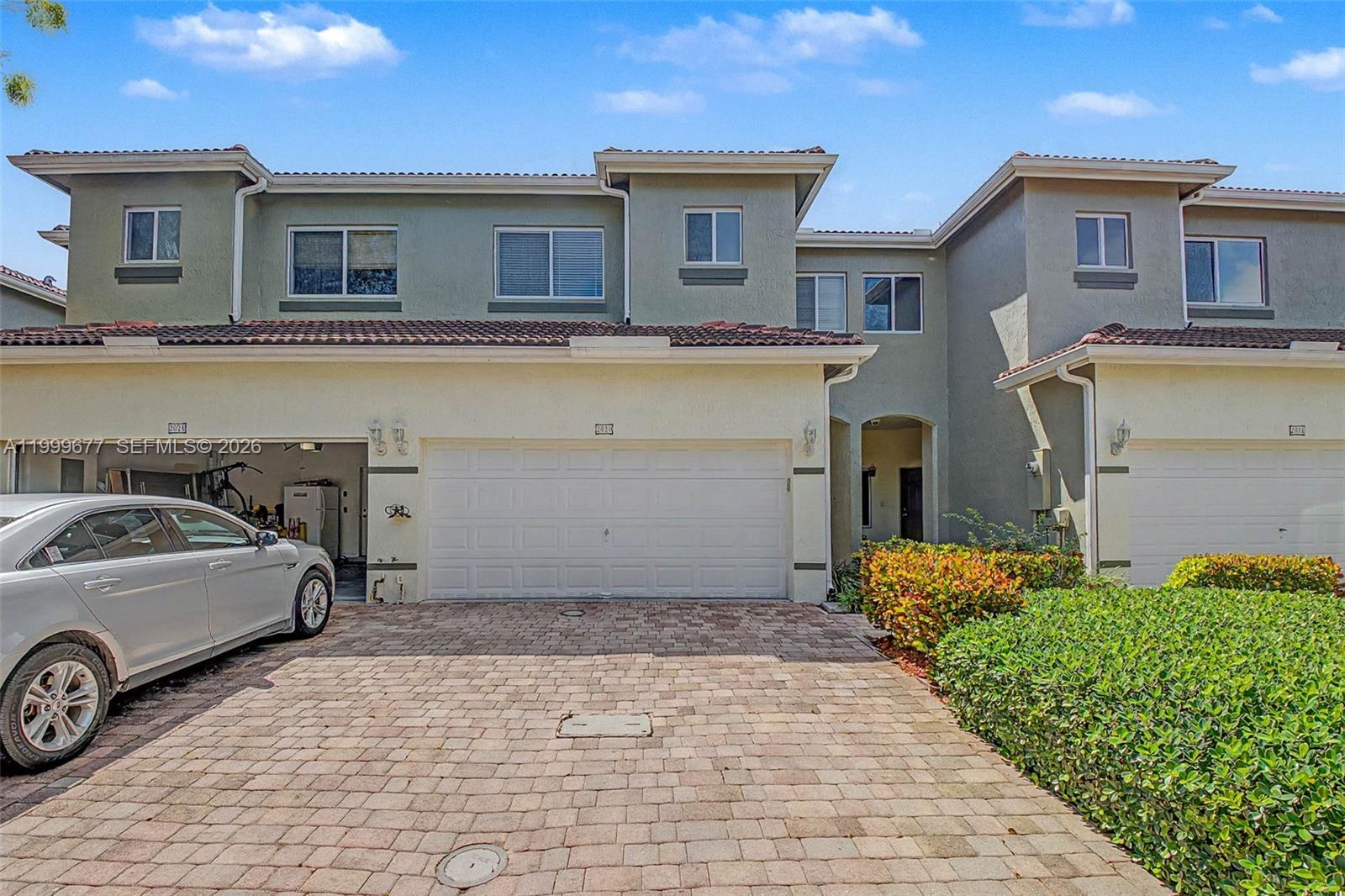 A two-story townhouse exterior features a paved driveway, a garage, and a small front garden — 2020 SE 23rd Ave, Homestead FL 33035, HOMESTEAD, FL