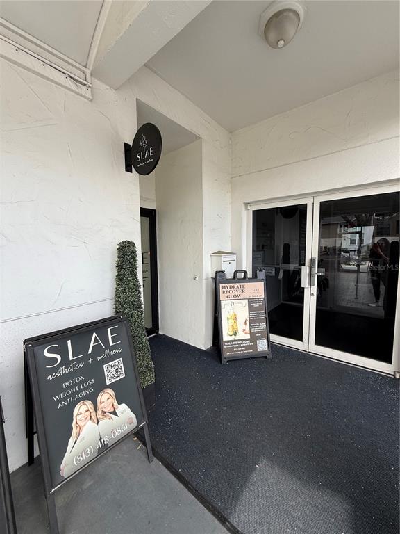 The exterior entrance of a commercial building features two sandwich board signs and glass doors — 2201 W SWANN AVENUE, TAMPA, FL