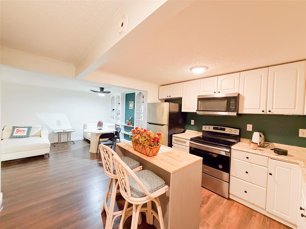 A kitchen with white cabinets, stainless steel appliances, and a wooden island with bar stools — 4219 E MICHIGAN STREET UNIT 4219, ORLANDO, FL