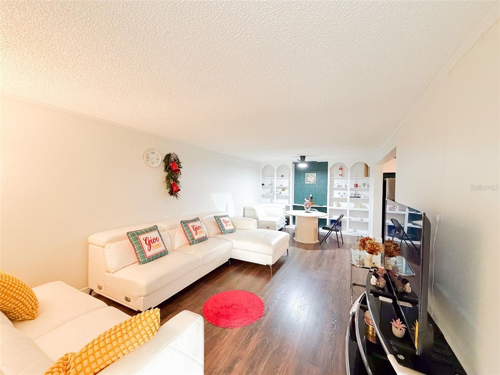 A living room features white sofas, wood-look flooring, a round red rug, and built-in shelving — 4219 E MICHIGAN STREET UNIT 4219, ORLANDO, FL