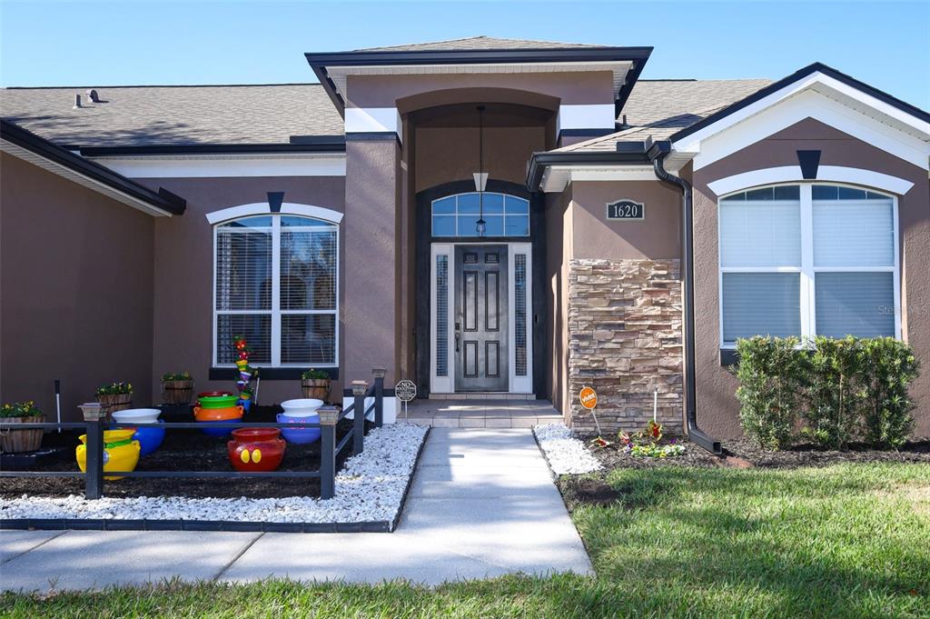 The front exterior of a single-story house features a stone facade, dark trim, and landscaping — 1620 PARKGLEN CIRCLE, APOPKA, FL