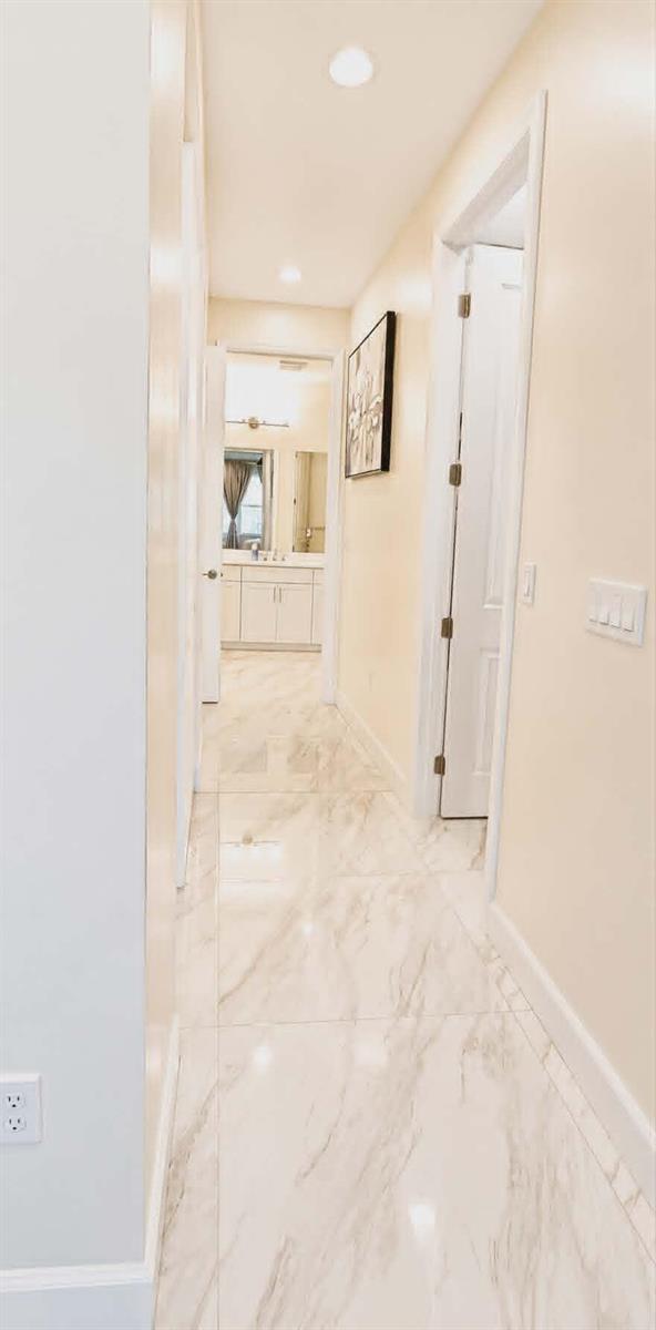 A hallway with light-colored walls and marble-patterned tile flooring leads toward a bathroom — 19179 Rolling Acres Road, Loxahatchee FL 33470, LOXAHATCHEE, FL