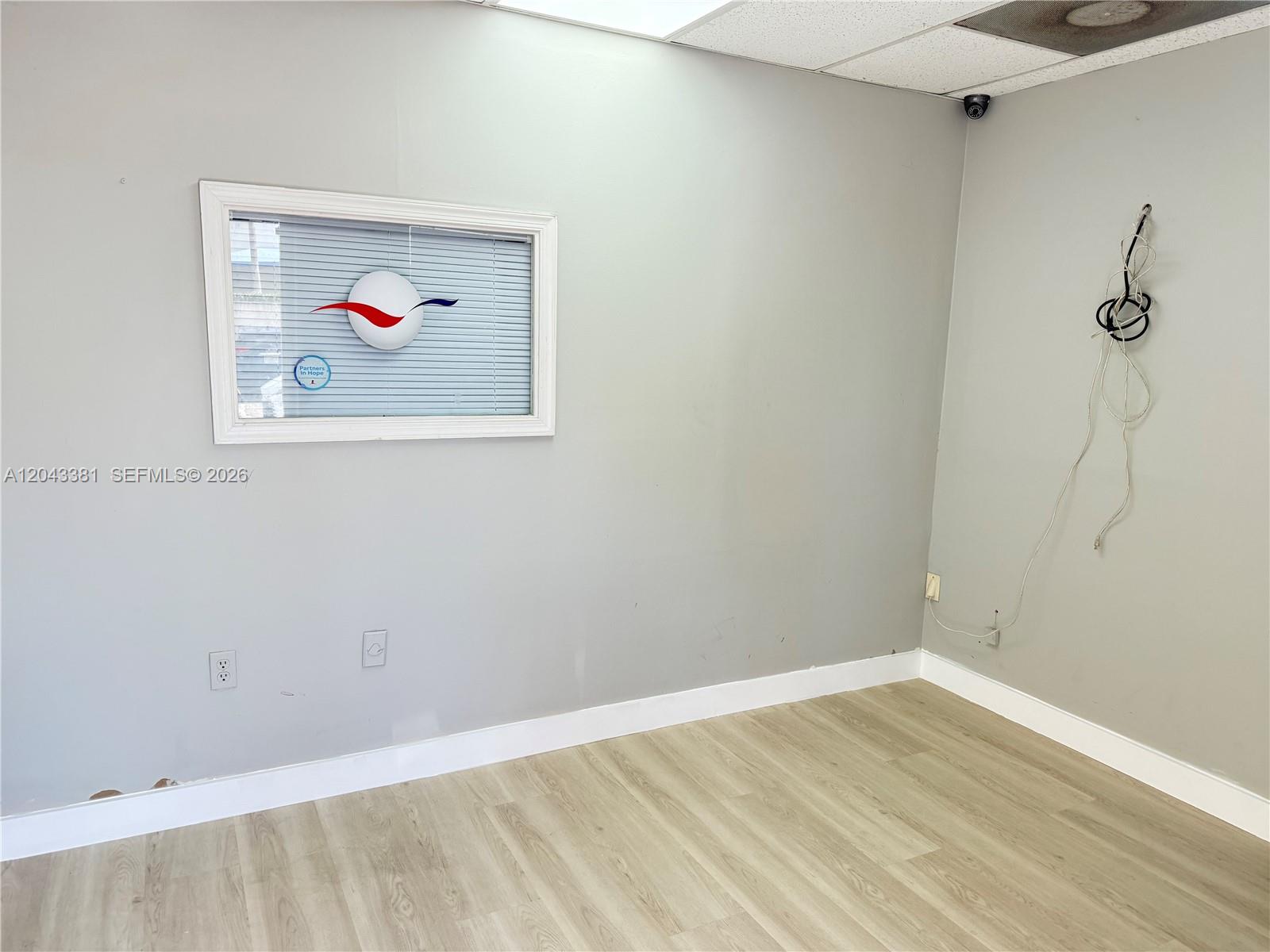 An empty office room features light gray walls, wood-look flooring, a window, and exposed wiring — 2630 NW 112th Ave # 2630, Doral FL 33172, DORAL, FL