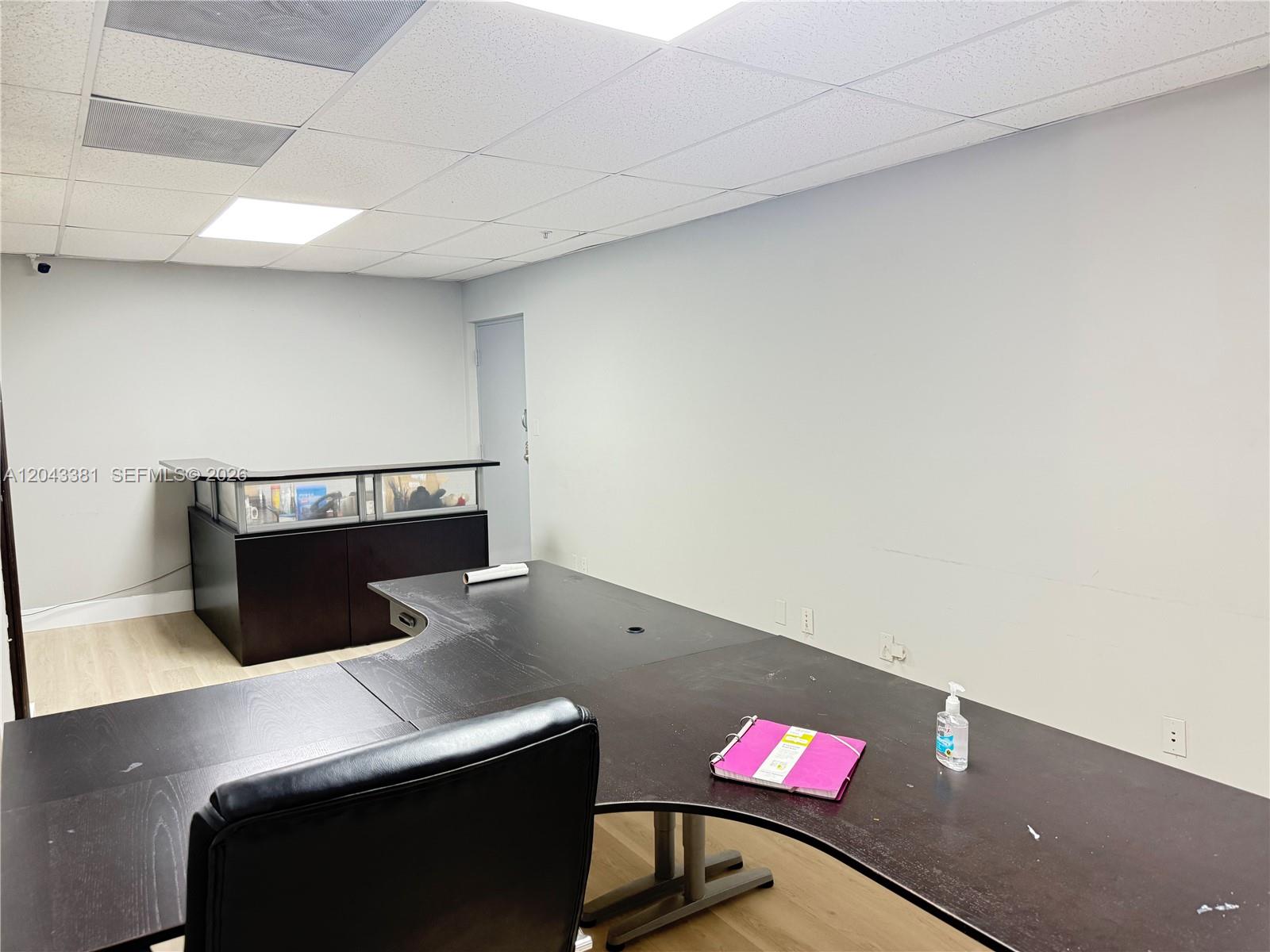 An office room features a dark L-shaped desk, a reception counter, and light wood flooring — 2630 NW 112th Ave # 2630, Doral FL 33172, DORAL, FL