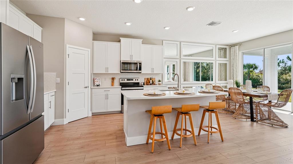 A modern kitchen features white cabinetry, a central island with bar stools, and wood flooring — 4249 SW 52ND LANE ROAD, OCALA, FL