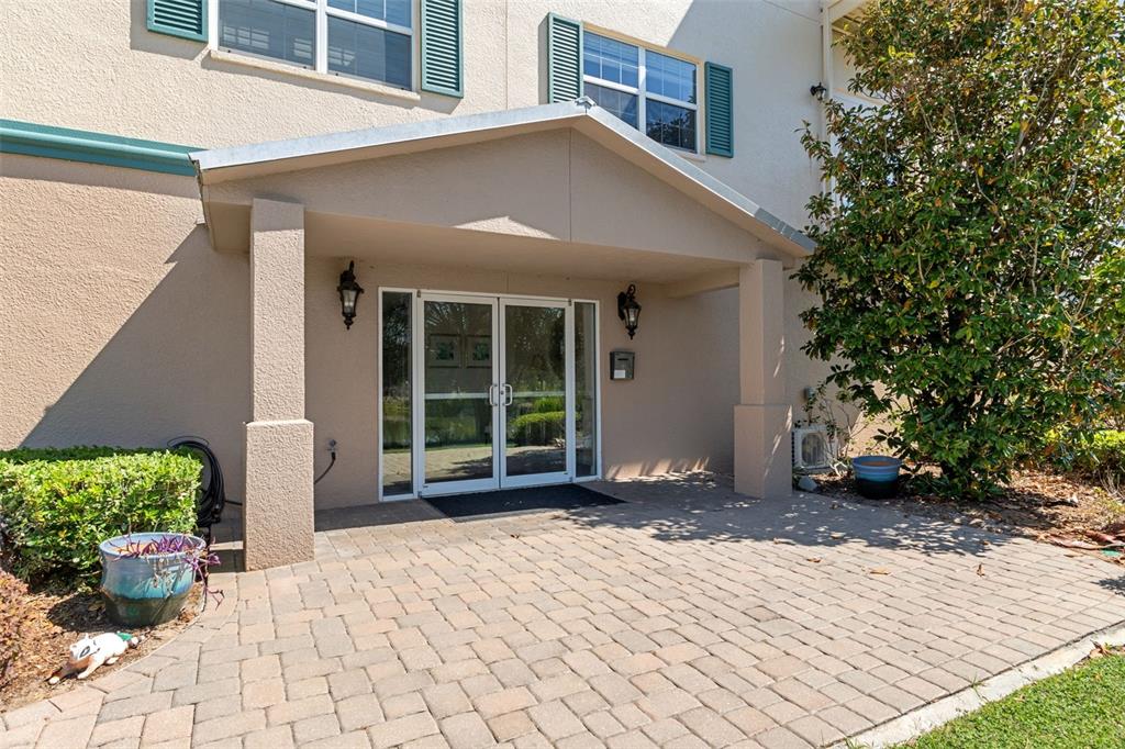 A paved patio leads to the glass double-door entrance of a beige building — 7986 SOUTHERN PINES DRIVE UNIT 536, BROOKSVILLE, FL