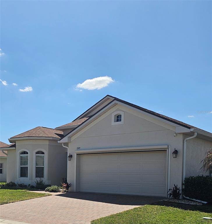 A single-story house with a beige stucco exterior, a two-car garage, and a brick driveway — 1347 OAKMONT DRIVE, WINTER HAVEN, FL