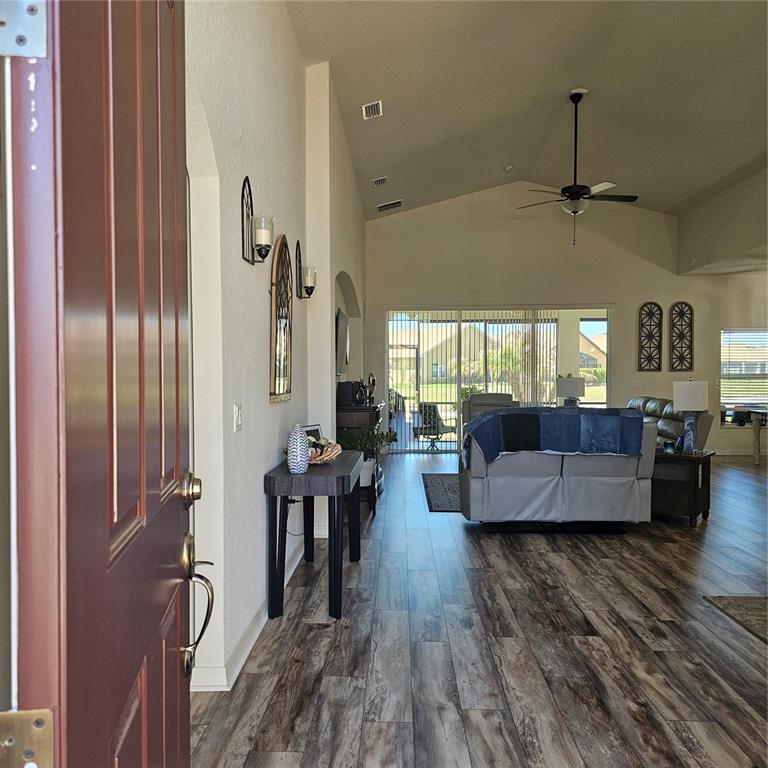 An open-concept living room with vaulted ceilings, wood-look flooring, and a view of the patio — 1347 OAKMONT DRIVE, WINTER HAVEN, FL