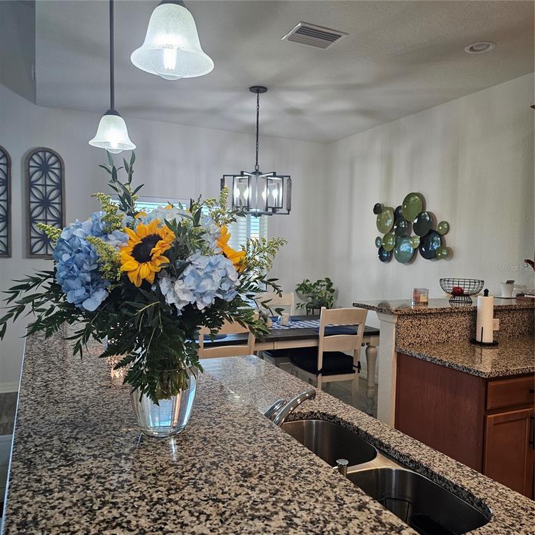 A kitchen island with a large flower arrangement overlooks a dining area with pendant lighting — 1347 OAKMONT DRIVE, WINTER HAVEN, FL