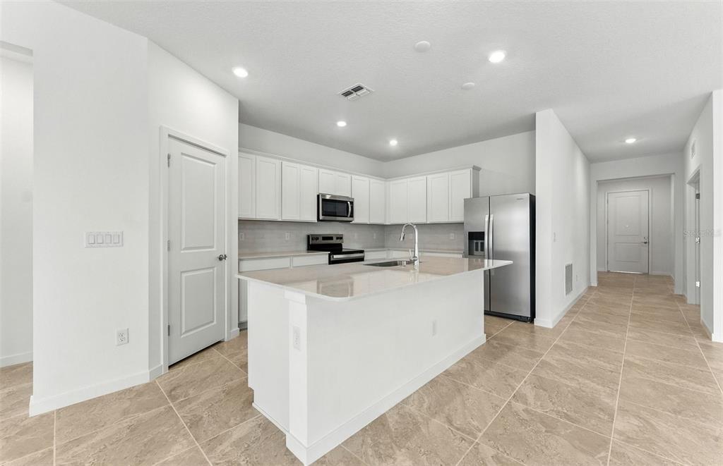 A modern kitchen features white cabinetry, stainless steel appliances, a center island, and tile flooring — 4018 BIG SKY DRIVE, SPRING HILL, FL