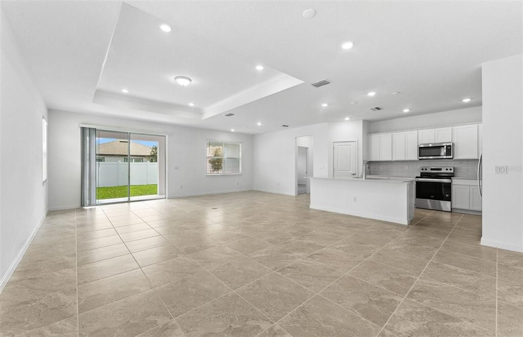 An open-concept kitchen and living area with white cabinets, tile flooring, and a sliding door — 4018 BIG SKY DRIVE, SPRING HILL, FL
