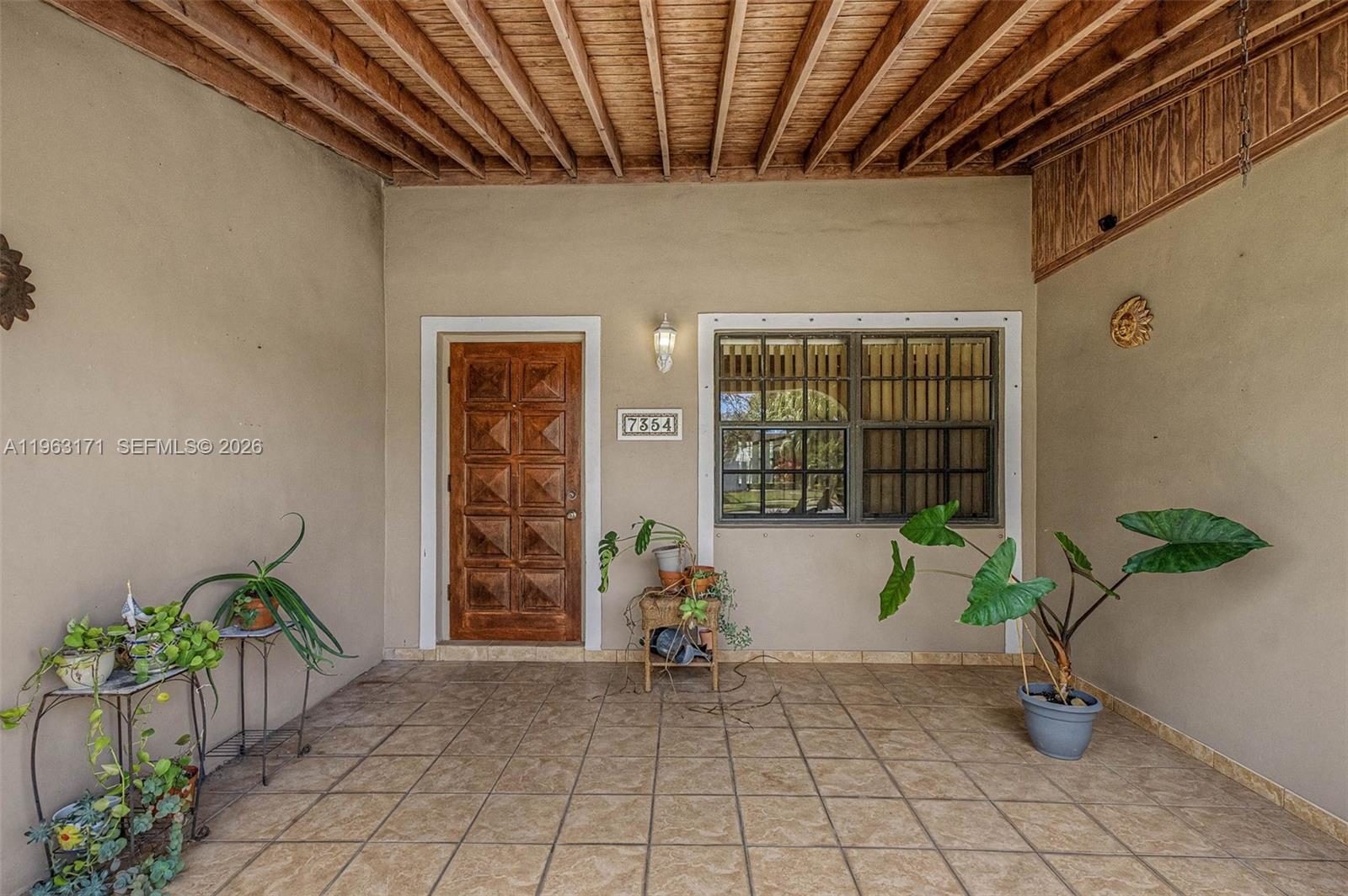 A covered porch features a tiled floor, a wooden door, and several potted plants — 7354 SW 135th Ct, Miami FL 33183, MIAMI, FL