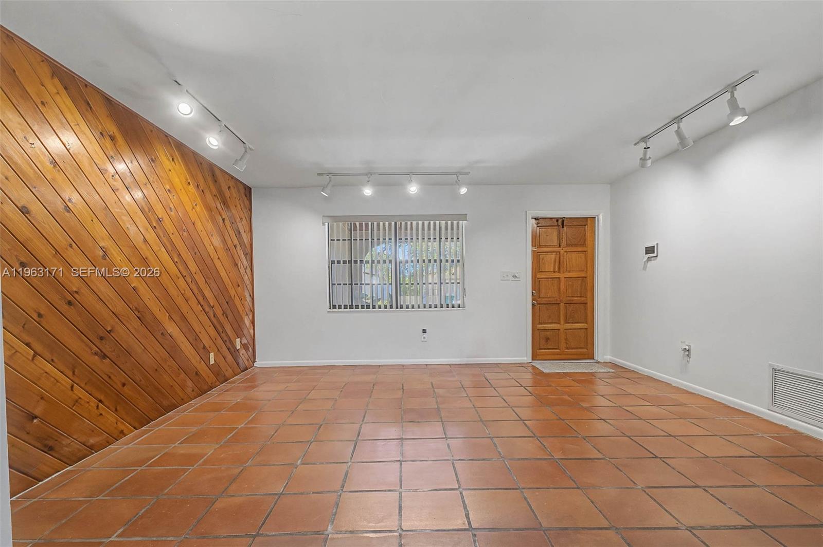 A room with terracotta tile flooring, white walls, a wood-paneled accent wall, and track lighting — 7354 SW 135th Ct, Miami FL 33183, MIAMI, FL