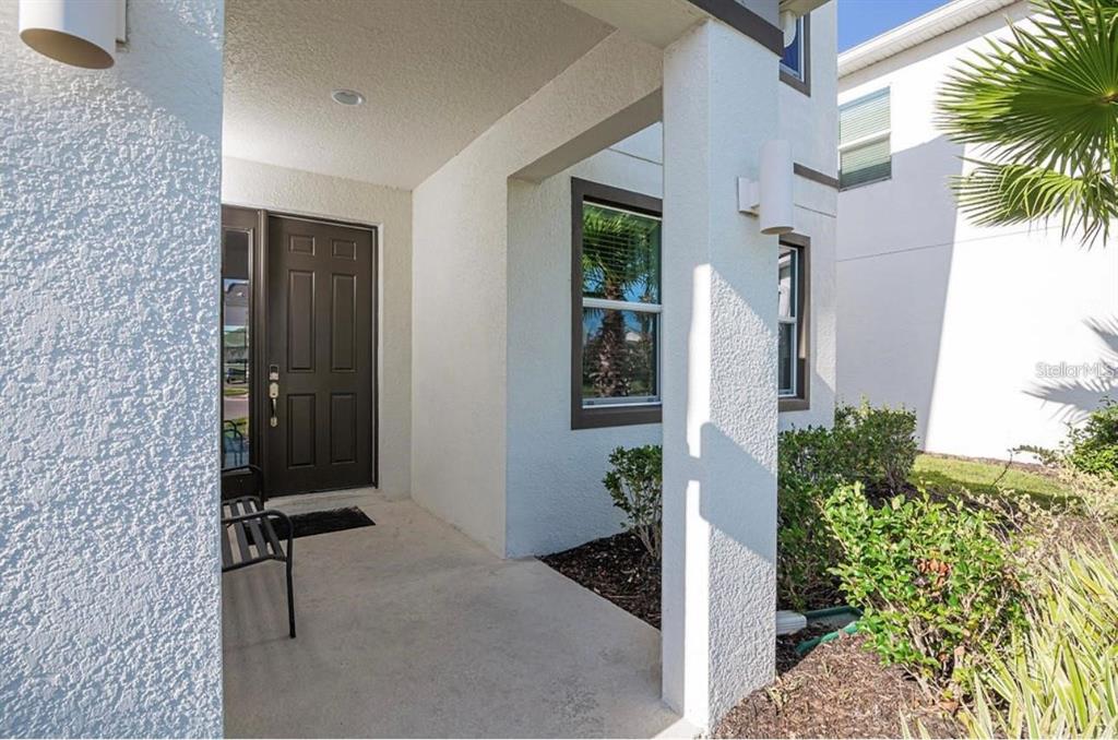 A covered front porch features a dark brown door, white stucco walls, and a metal bench — 2659 CALISTOGA AVENUE, KISSIMMEE, FL