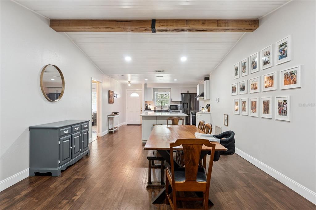 A dining area with a wooden table and beam ceiling opens into a modern kitchen — 1404 BEVERLY LANE, CASSELBERRY, FL