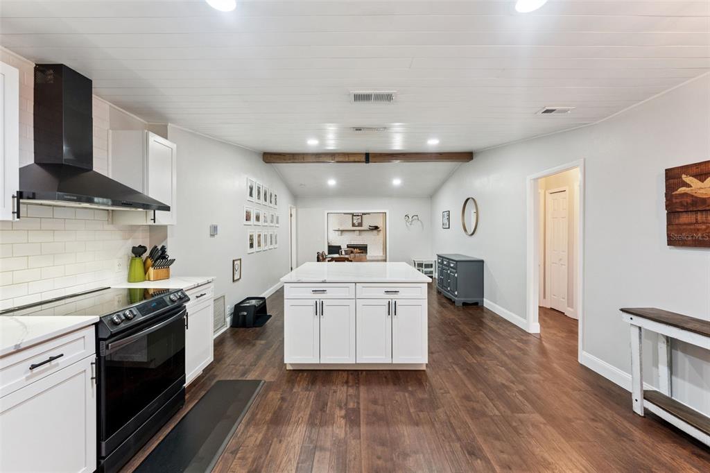 A kitchen features white cabinets, a central island, a black range, and wood-look flooring — 1404 BEVERLY LANE, CASSELBERRY, FL