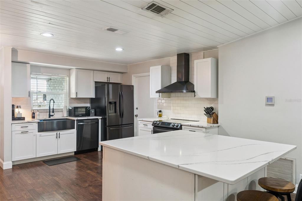 A modern kitchen features white cabinets, a large island, dark appliances, and wood-look flooring — 1404 BEVERLY LANE, CASSELBERRY, FL