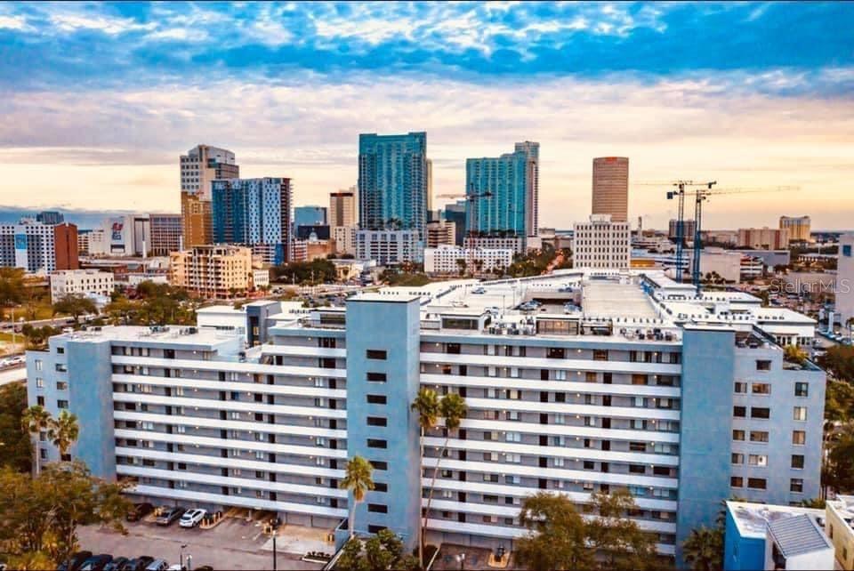 An exterior view of a multi-story apartment building with a parking garage and city skyline — 201 W LAUREL STREET UNIT 712, TAMPA, FL