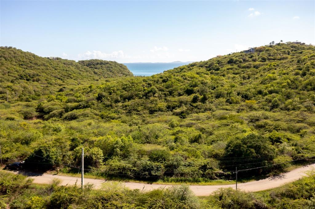 An elevated view shows a dirt road curving through a lush, hilly landscape toward the ocean — 10 SOUTHEAST HARBOUR ESTATES, CULEBRA, PR