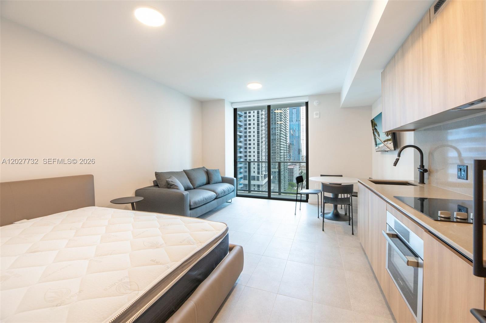 A studio apartment features a bed, a gray sofa, a dining set, and a kitchenette — 121 NE 5th St # 1809, Miami FL 33132, MIAMI, FL