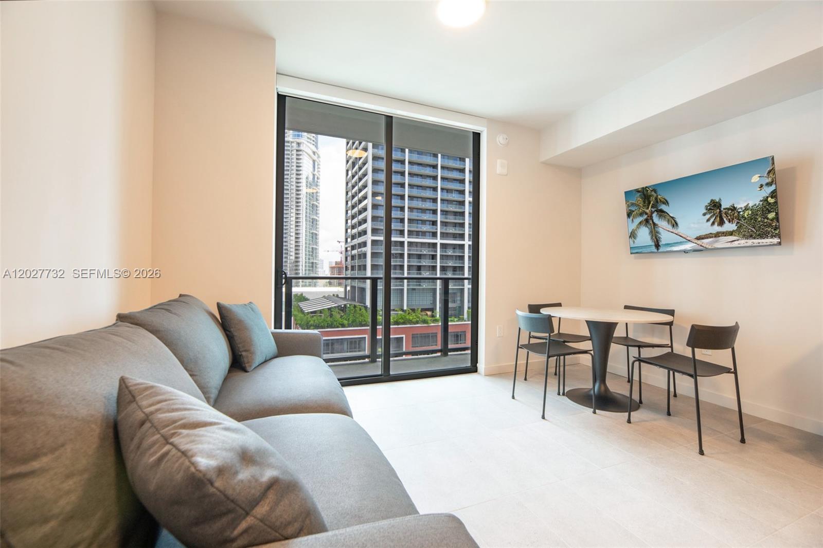 A living and dining area features a grey sofa, a round table, and balcony views — 121 NE 5th St # 1809, Miami FL 33132, MIAMI, FL