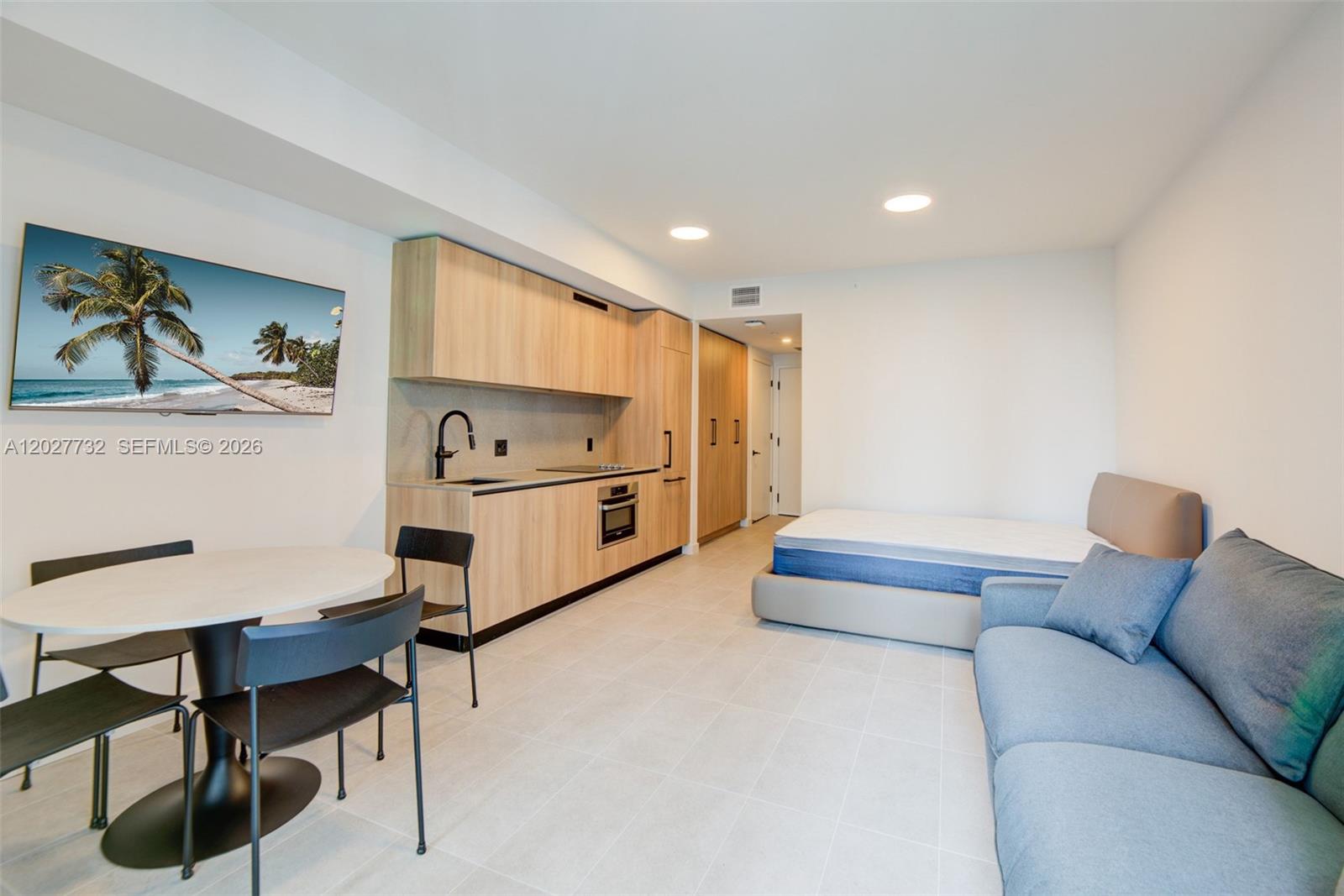 This studio apartment features a kitchenette with light wood cabinetry, a dining area, and a bed — 121 NE 5th St # 1809, Miami FL 33132, MIAMI, FL