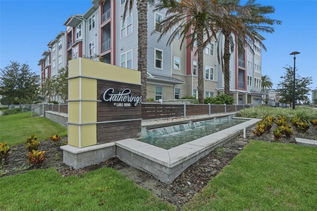 A modern apartment building sign stands beside a small water feature and palm trees — 7505 LAUREATE BOULEVARD UNIT 2408, ORLANDO, FL