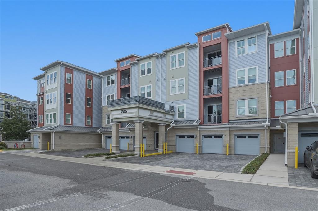 A multi-story apartment building with a covered entrance, gray garage doors, and balconies — 7505 LAUREATE BOULEVARD UNIT 2408, ORLANDO, FL