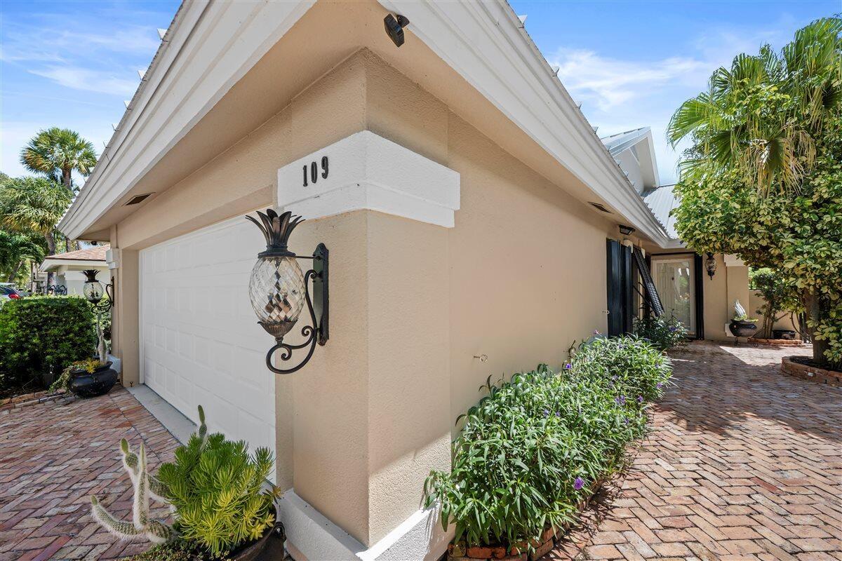 A beige house exterior features a white garage door, brick driveway, and pineapple-shaped wall sconce — 109 Seashore Drive, Jupiter FL 33477, JUPITER, FL